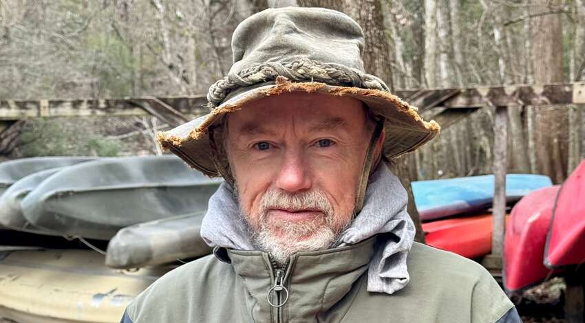 Lars Andersen outdoors in front of a stand of canoes
