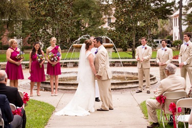 Couple kiss in front of fountain, surrounded by wedding party