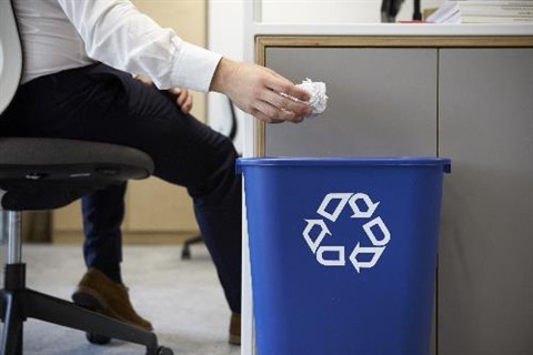 guy recycling paper at work in blue recycle bin