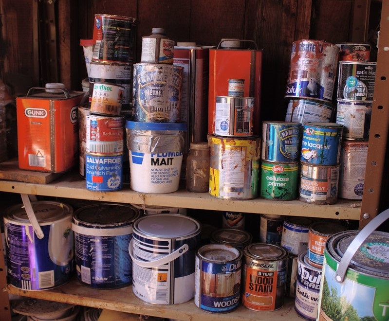 various paint cans on a shelf in a shed
