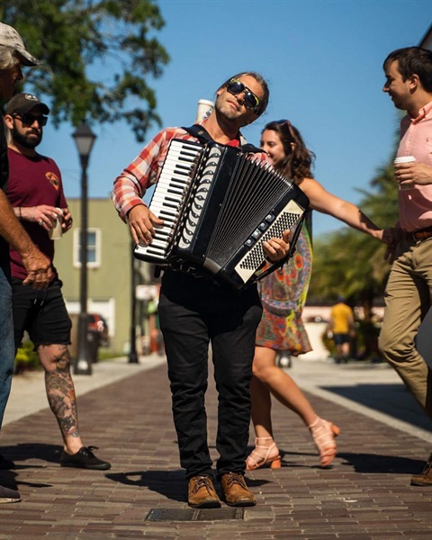 A musician playing an accordion outdoors on a brick sidewalk.
